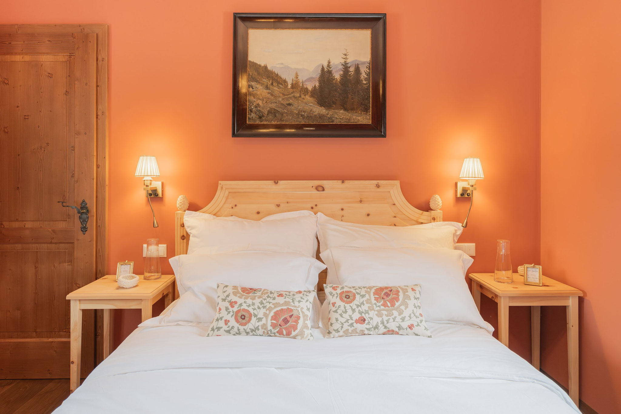 Schlafzimmer mit Zirbenbett, warmem Terracotta-Farbton und Bergbild