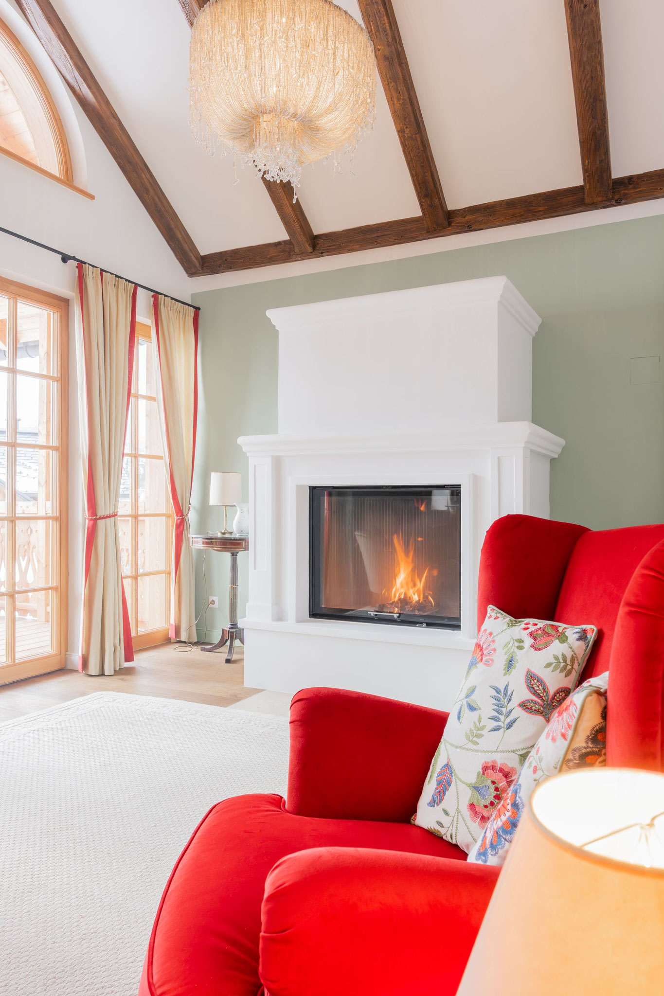Wohnsalon mit offenem Kamin, rotem Sessel, salbeifarbenen Wänden und Holzbalkendecke